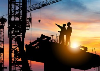 Silhouette of Engineer and worker checking project at building site background, construction site at sunset in evening time.